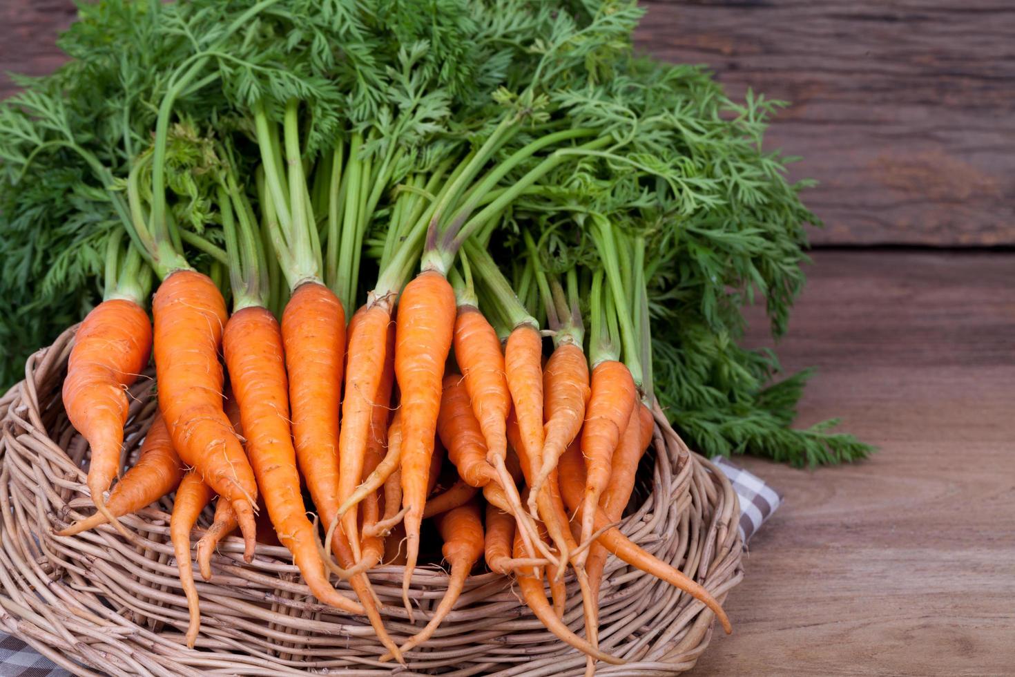 massa färska morötter med gröna blad över träbakgrund foto