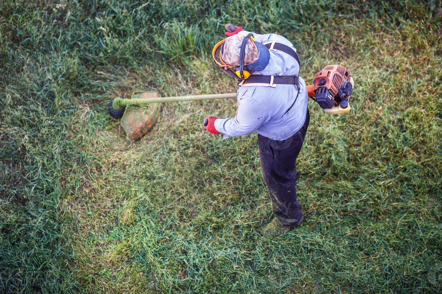 ovanifrån fett smutsig gräsklippare man arbetare klippa torrt gräs med gräsklippare. foto