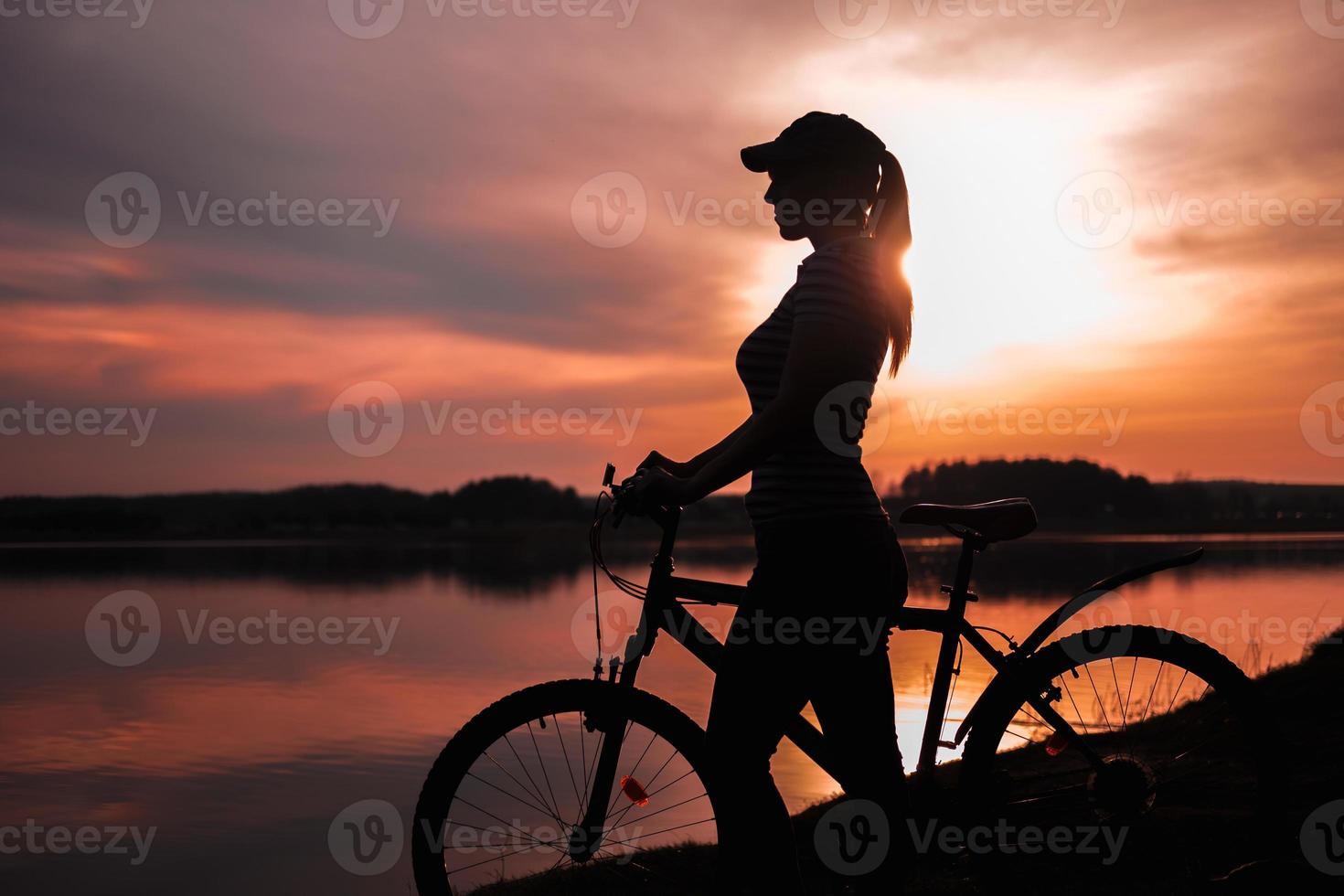 sommar siluett landskap. flicka med en cykel vid sjön mot bakgrund av den nedgående solen, den röda solnedgången foto