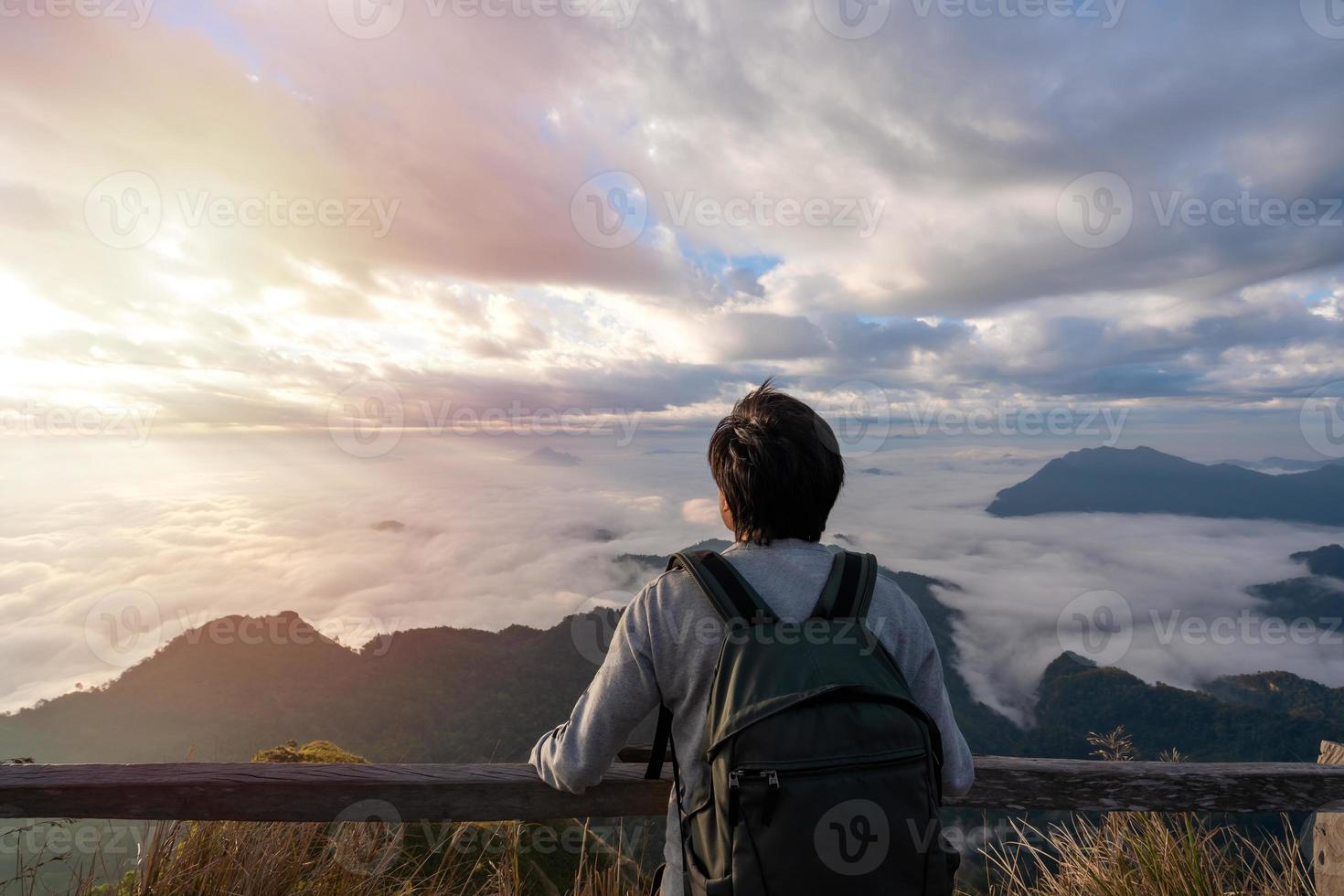 ung man resenärer tittar på soluppgången och havet av dimman på berget på morgonen, resa livsstilskoncept foto