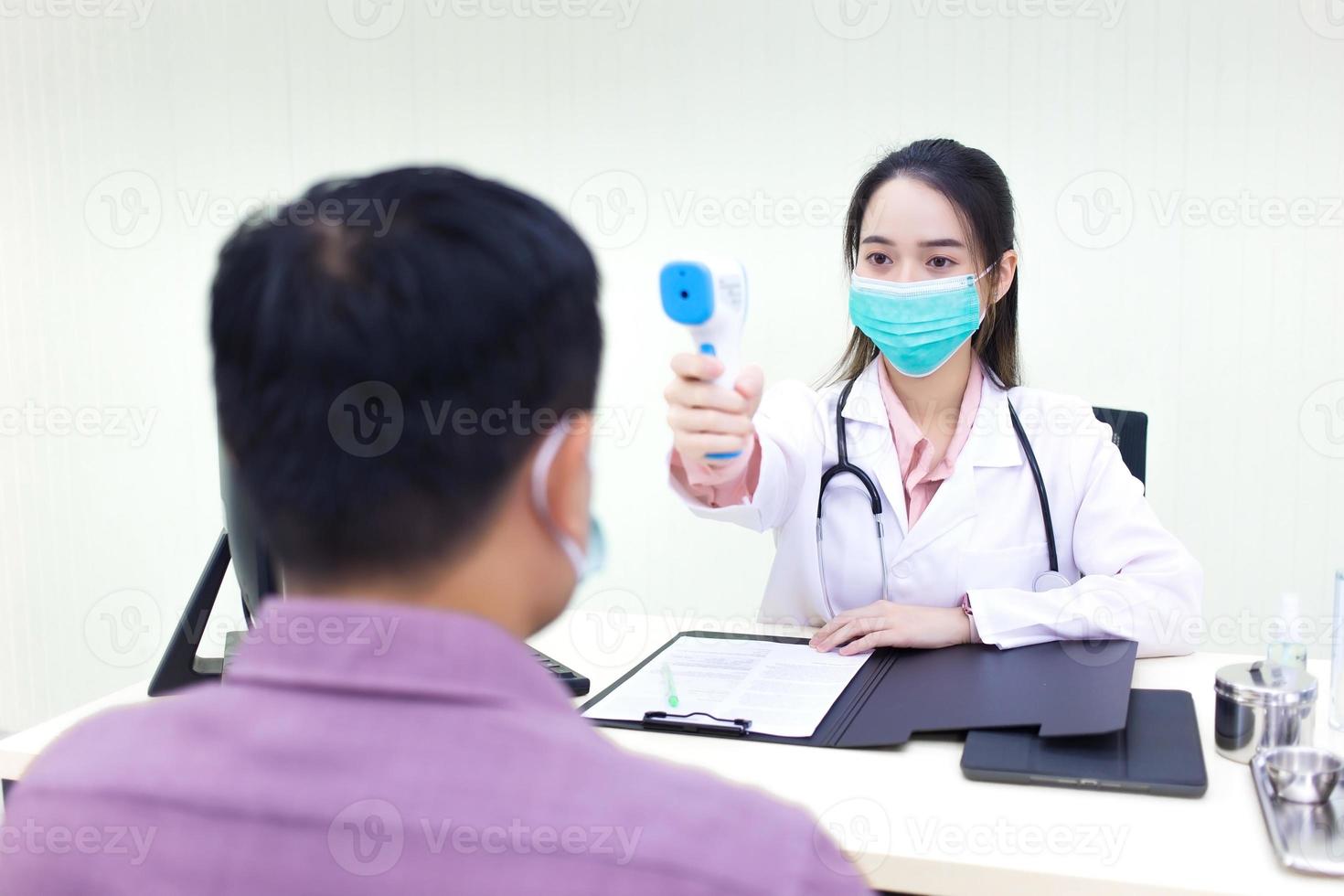 asiatisk kvinna läkare använder en infraröd panna termometer för att mäta kroppstemperatur foto