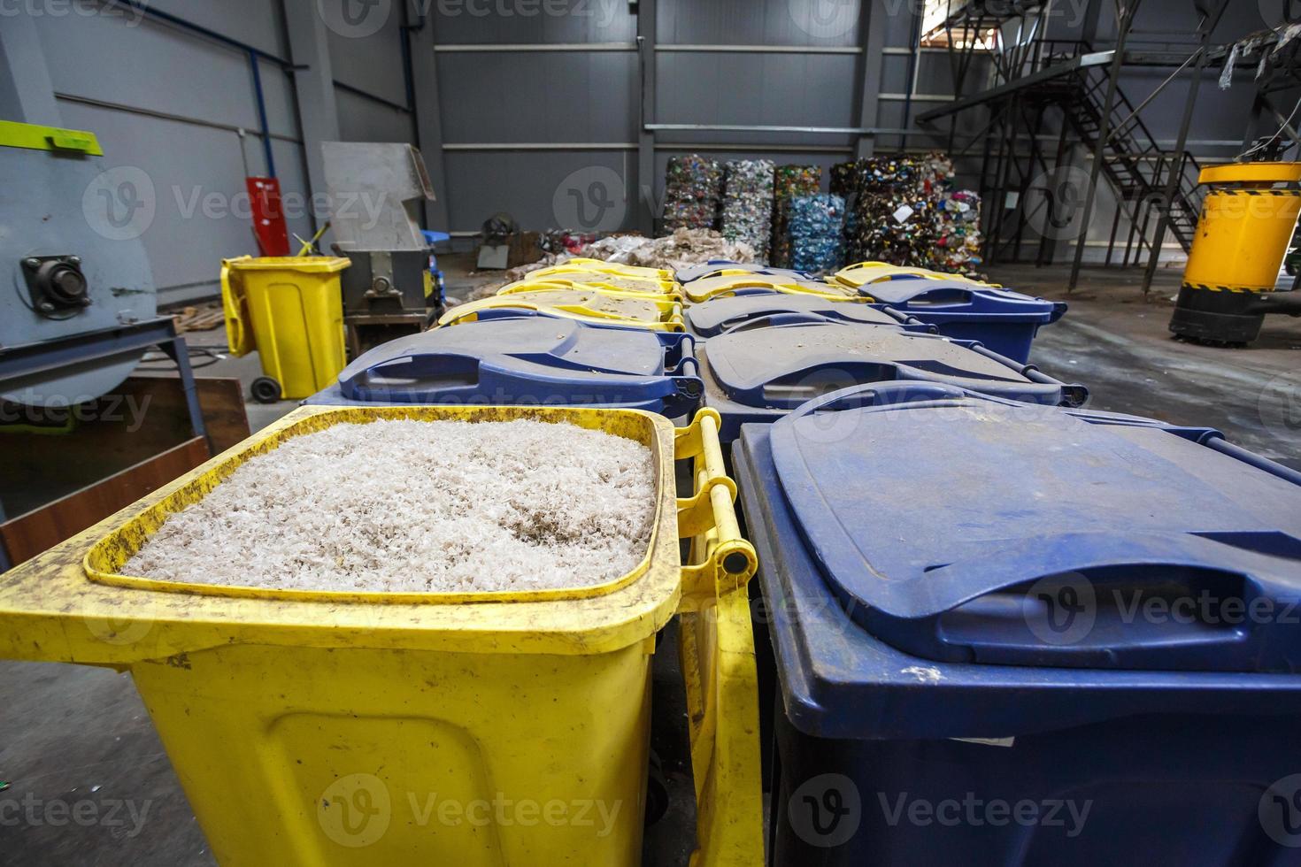 behållare med strimlad plast förberedda för vidarebearbetning omsmältning och återvinning med rivare och balar med plastavfall i bakgrunden. modern anläggning för bearbetning och sortering av sopor foto