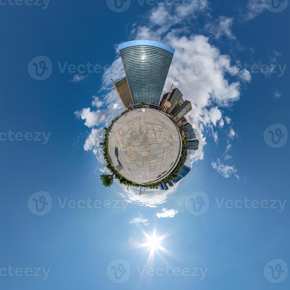 liten planet i blå himmel med moln i centrum nära moderna skyskrapor eller kontorsbyggnader. transformation av sfäriskt 360 panorama i abstrakt flygvy. foto