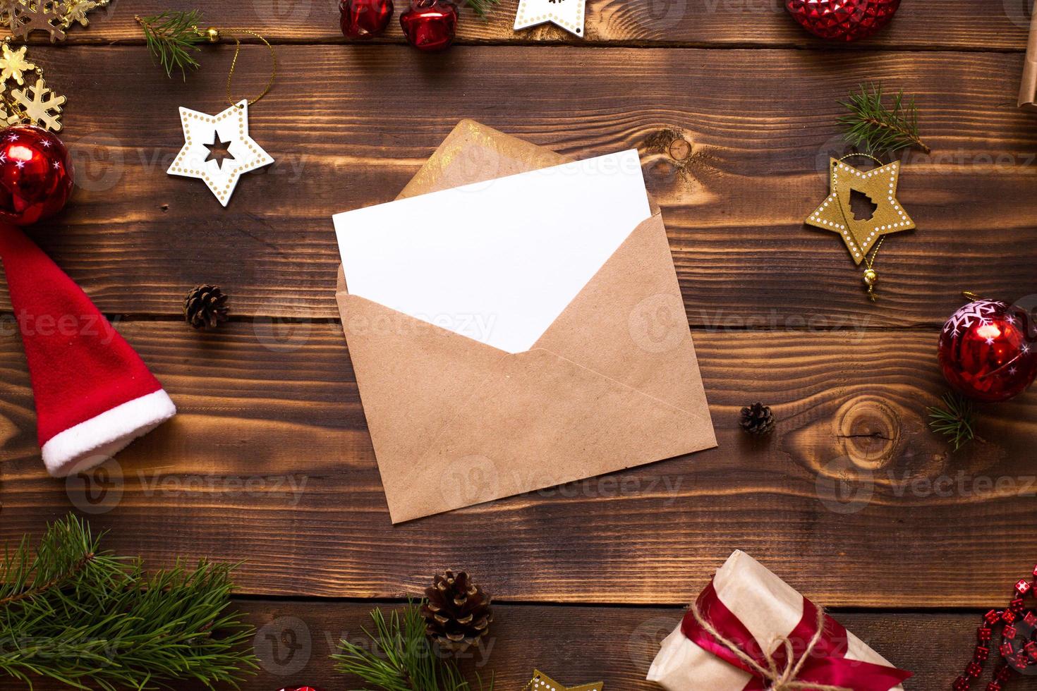postkuvert av hantverkspapper med ett vitt ark för text på en träbakgrund med juldekor. ett brev till jultomten, en önskelista, en nyårsdröm, en present. platt låg, kopiera utrymme foto