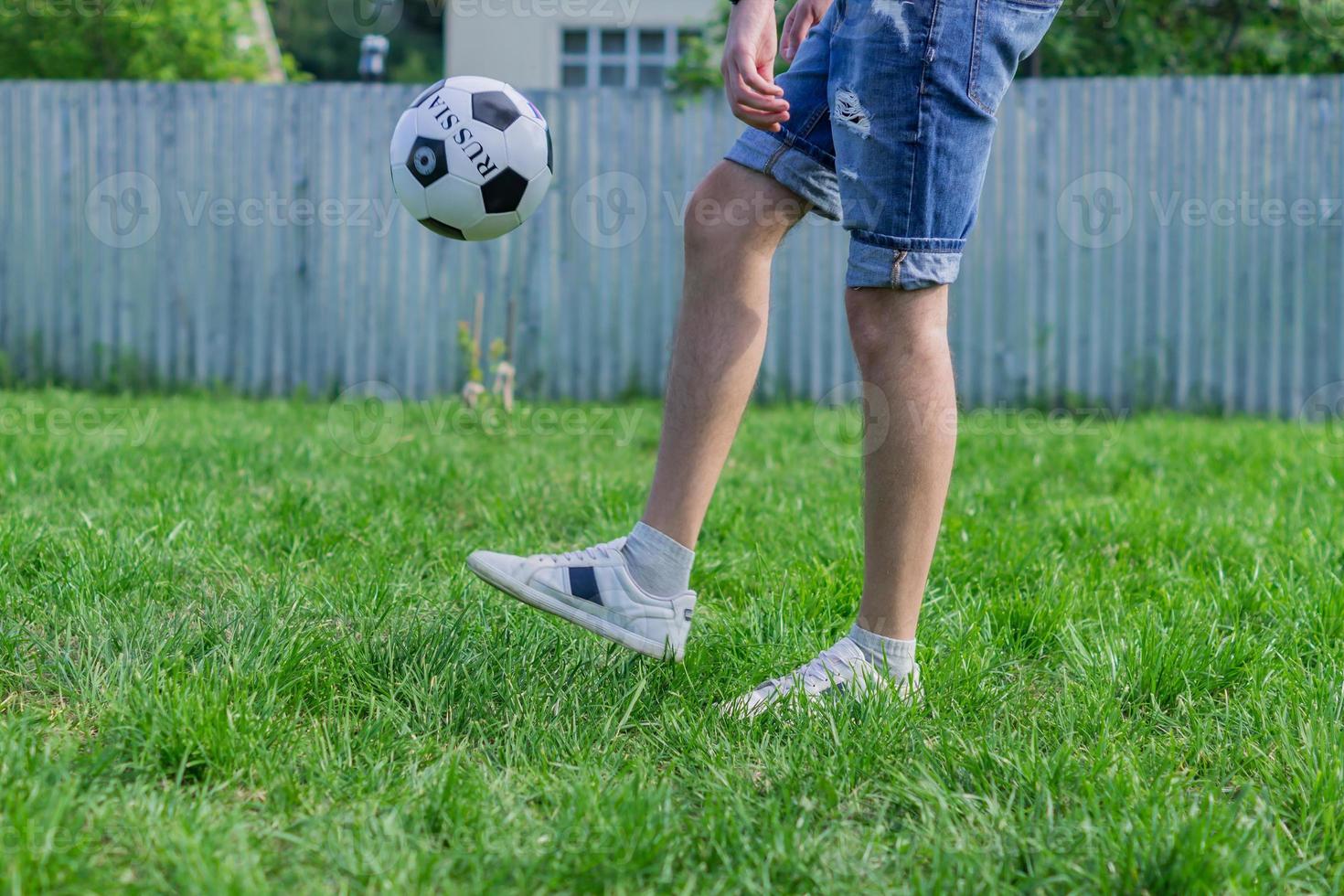 ung man i jeansjeans och vita sneakers som spelar fotboll utomhus. amatör fotbollsspelare mint bollen foto