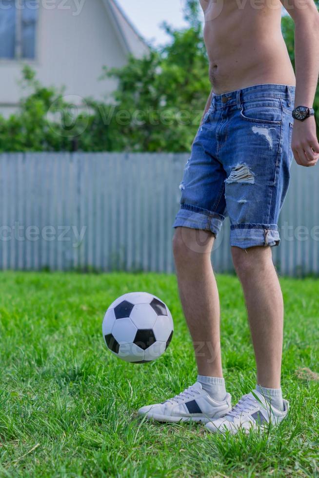 ung man i jeansjeans och vita sneakers som spelar fotboll utomhus. amatör fotbollsspelare mint bollen foto