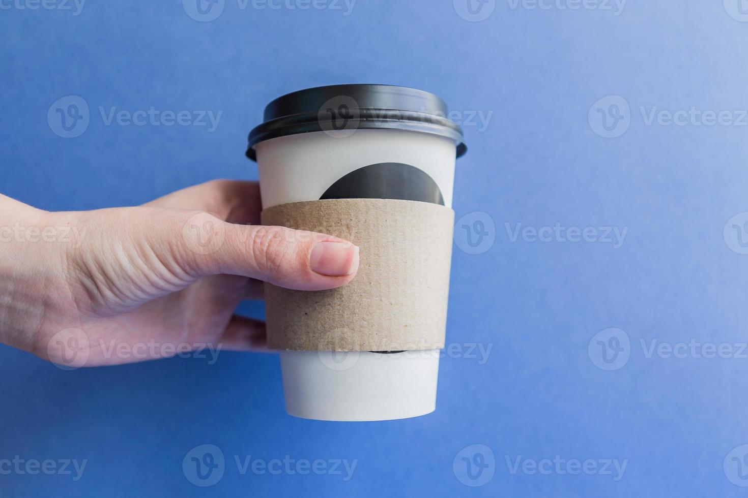 vit pappers kraft engångskopp för kaffe med svart plastlock i en kvinnlig hand. kaffe att gå på blå bakgrund. foto