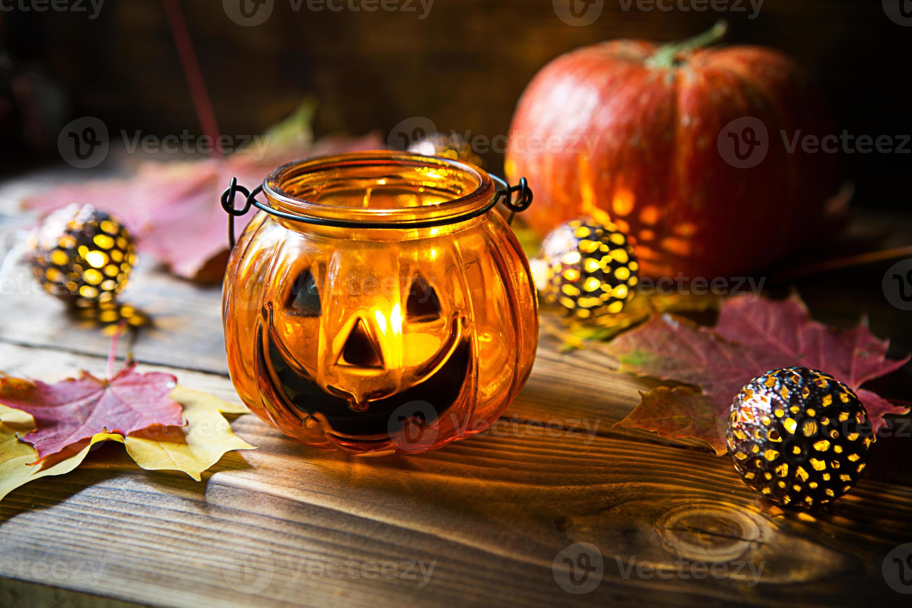 lampa pumpa med ögon och mun tillverkad av glas och naturlig orange pumpa  på en trä- tabell med gul och röd lönn löv. halloween, värma höst atmosfär.  runda krans, ljus i en