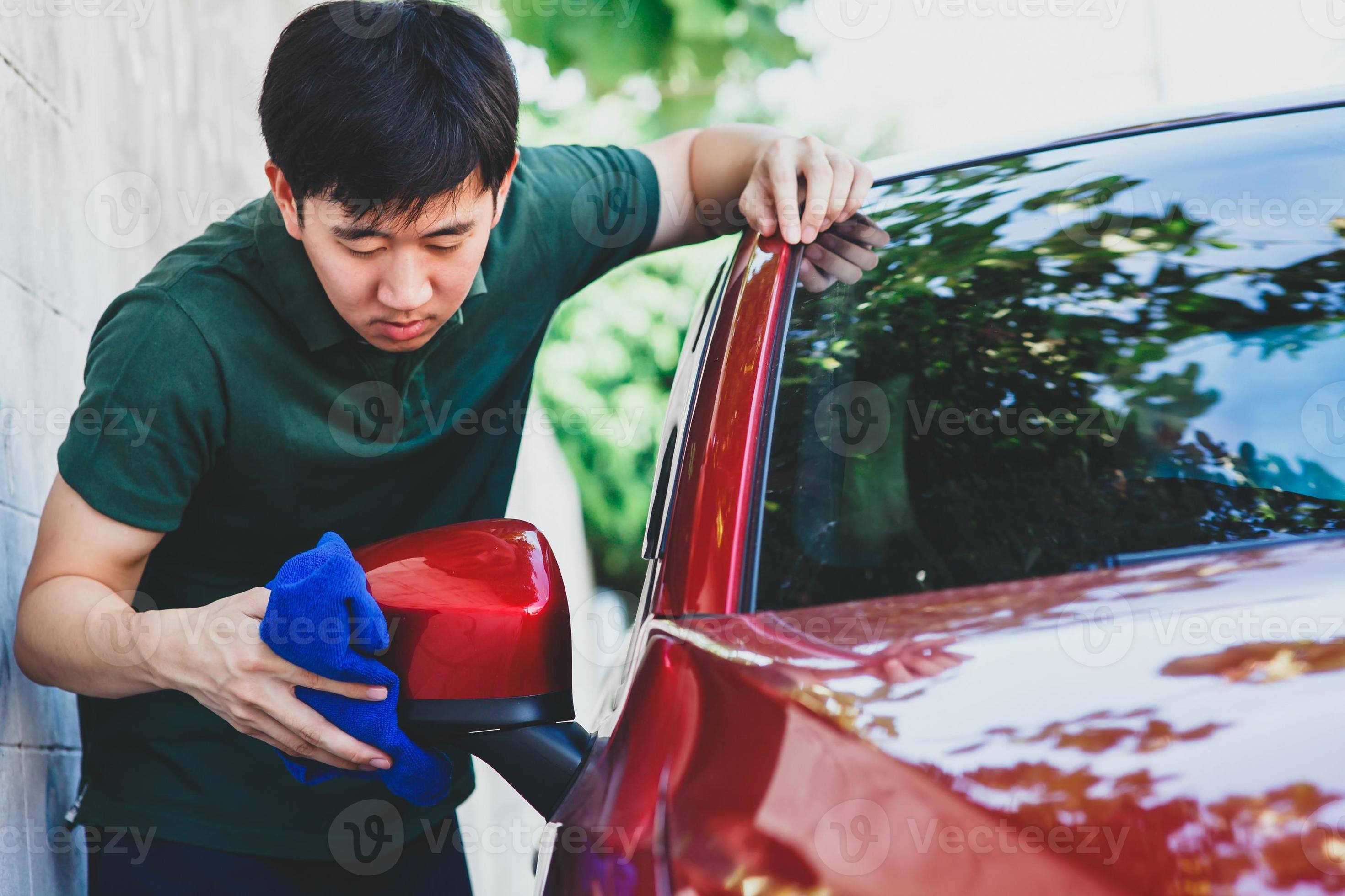 ung asiatisk man i enhetlig rengöring och tvätt av en bil foto