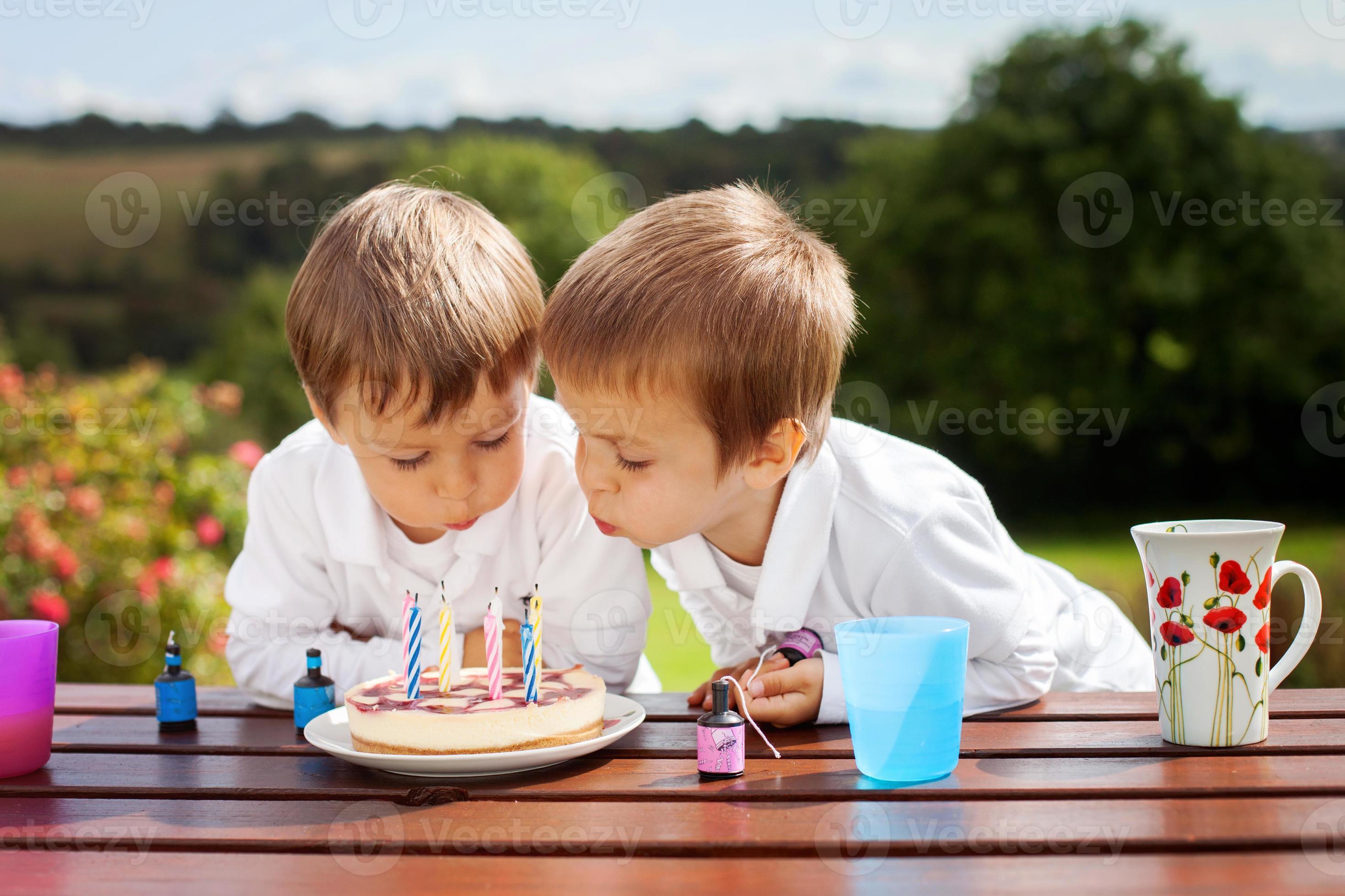 bedårande pojkar, blåser ljus på en födelsedagstårta foto
