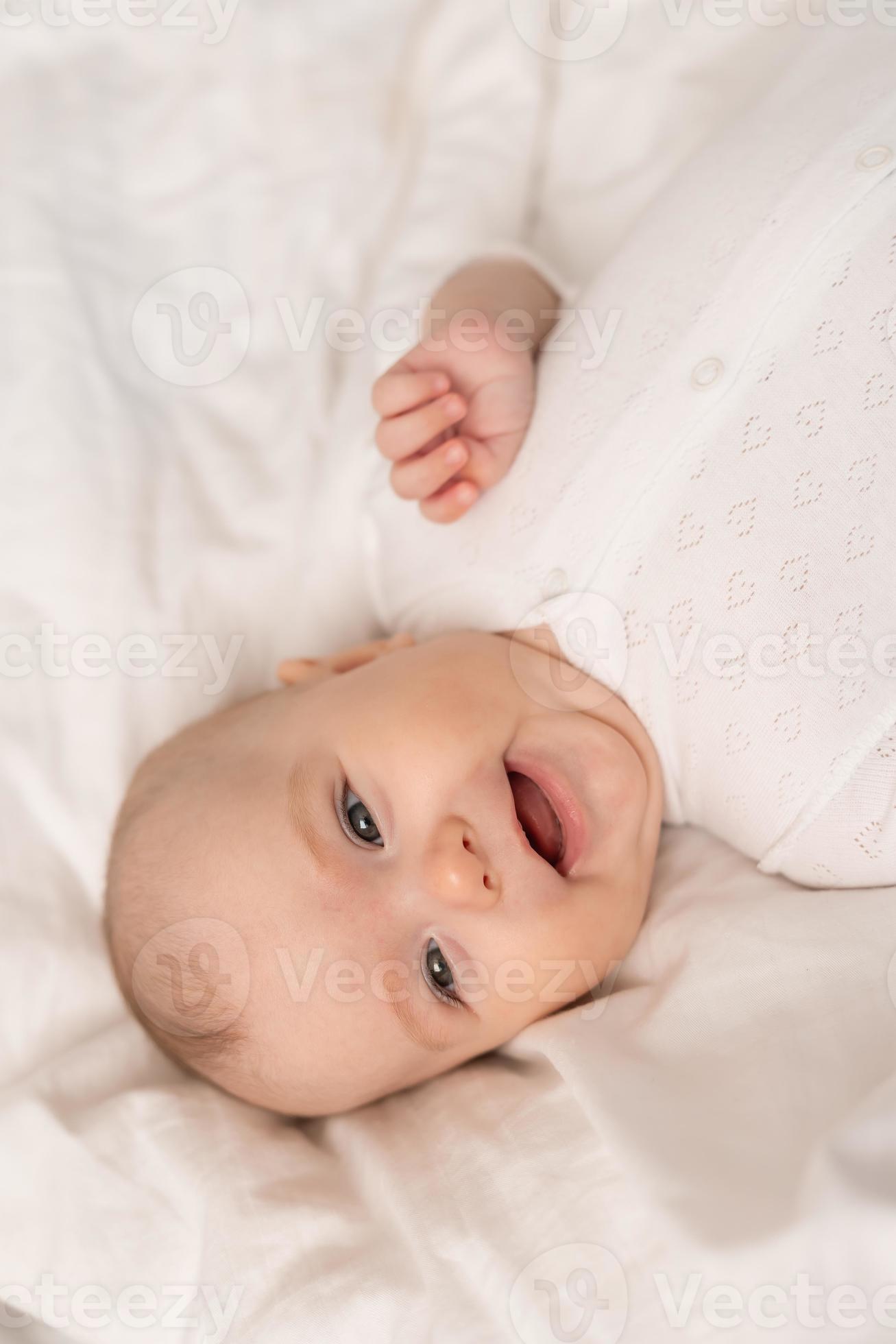 porträtt av en söt bebis i en vit kroppsdräkt på en säng på Hem med vit  sängkläder. nyfödd bebis på Hem, Lycklig moderskap. hög kvalitet Foto  17725030 Arkivfoto på Vecteezy