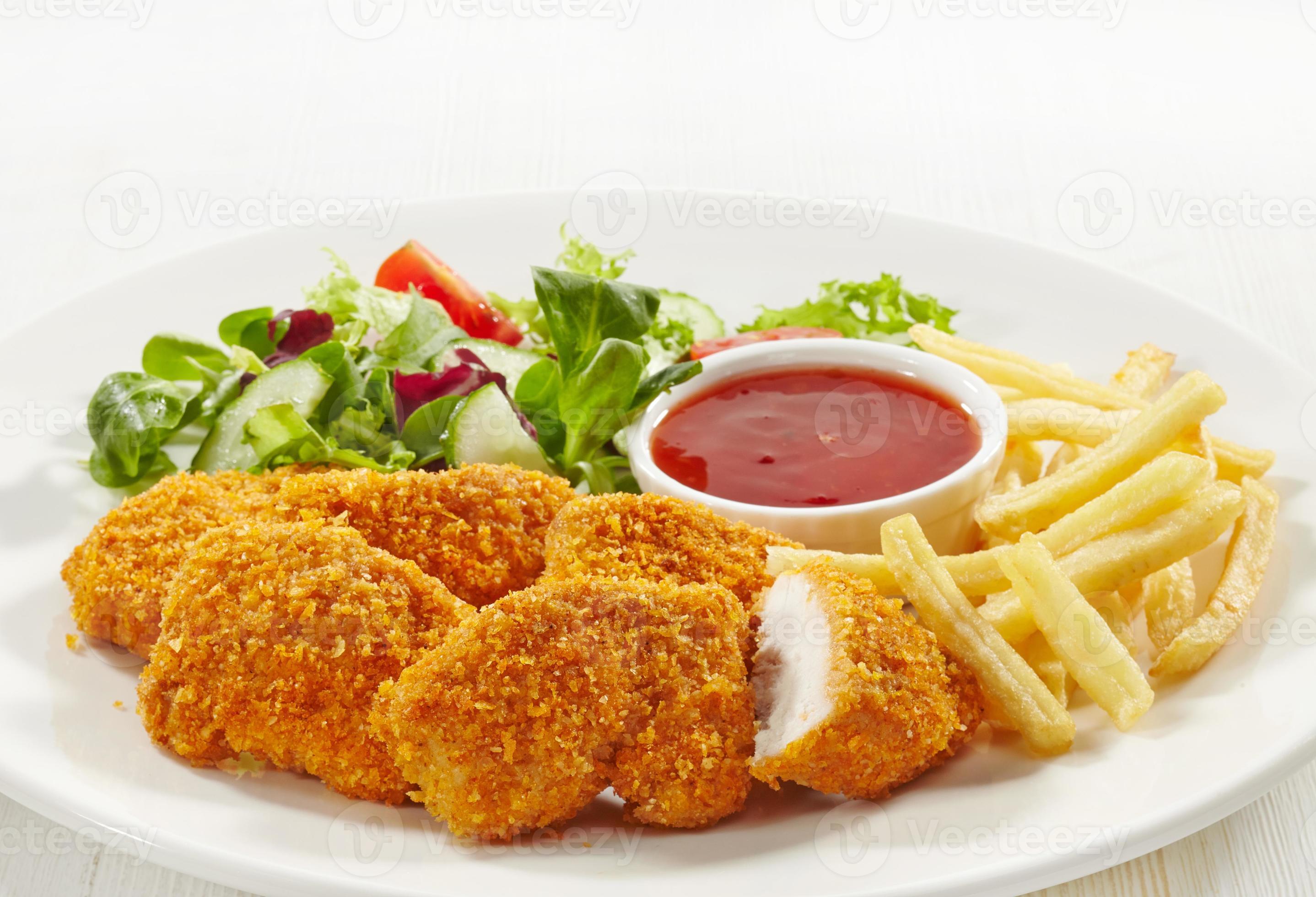 kyckling nuggets chips sallad och röd sås på en vit platta foto