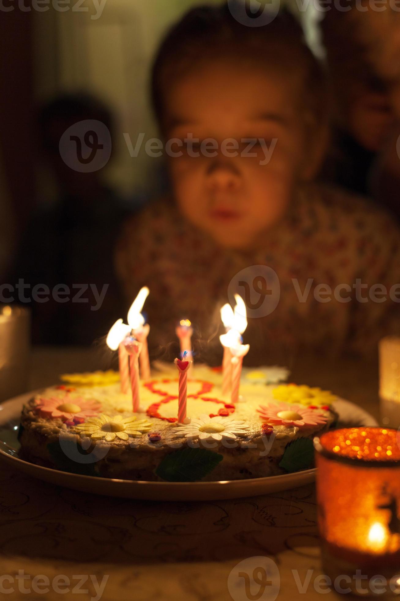 liten flicka som blåser ut ljus på födelsedagstårta foto