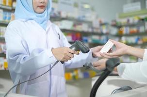 kvinnlig muslimsk farmaceut som skannar streckkoden i ett modernt apotek. foto