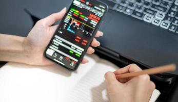 kvinnlig handlare investerare mäklare analytiker som håller en smartphone i handen analyserar aktiemarknadshandelsdiagram indexerar data som kontrollerar priset med hjälp av mobil börsapplikation. foto