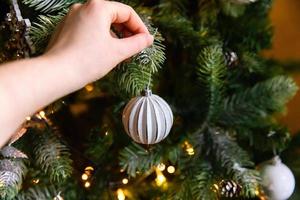 kvinna hand dekorera julgran. julgran med vit och silver dekorationer, prydnadssaker leksak och boll. modern inredning i klassisk stil. julafton hemma, dags för firande. foto
