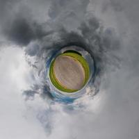 liten planet sfärisk panorama 360 grader. sfärisk flygfoto i fältet med svarta fantastiska moln före stormen. utrymmets krökning. ljus vs mörker foto