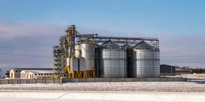 agro silos spannmålsmagasin hiss i vinterdag i snöiga fält. silos på en produktionsanläggning för jordbruksbearbetning för bearbetning av kemtvätt och lagring av jordbruksprodukter, mjöl, spannmål och spannmål. foto