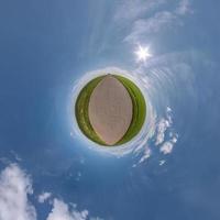 grön liten planet i blå himmel med sol och vackra moln. transformation av sfäriskt panorama 360 grader. sfärisk abstrakt flygfoto. utrymmets krökning. foto