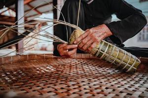 fokusera gammal kvinna med traditionell vietnamesisk klänning ao ba ba att göra, slå in tet tårta, det vietnamesiska månnyåret tet mat utomhus för händer. foto