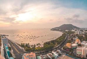 vung tau stadens flygfoto med vacker solnedgång och så många båtar. panoramautsikt över kustnära vung tau från ovan, med vågor, kustlinje, gator, kokospalmer och tao phung-berget i vietnam. foto