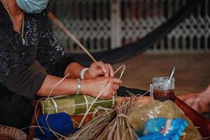 fokusera gammal kvinna med traditionell vietnamesisk klänning ao ba ba att göra, slå in tet tårta, det vietnamesiska månnyåret tet mat utomhus för händer. foto