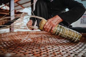 fokusera gammal kvinna med traditionell vietnamesisk klänning ao ba ba att göra, slå in tet tårta, det vietnamesiska månnyåret tet mat utomhus för händer. foto