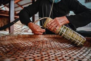 fokusera gammal kvinna med traditionell vietnamesisk klänning ao ba ba att göra, slå in tet tårta, det vietnamesiska månnyåret tet mat utomhus för händer. foto