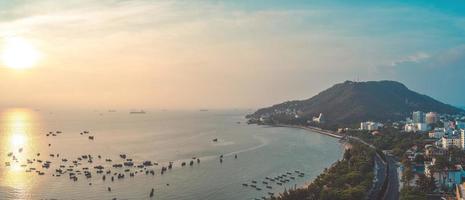 vung tau stadens flygfoto med vacker solnedgång och så många båtar. panoramautsikt över kustnära vung tau från ovan, med vågor, kustlinje, gator, kokospalmer och tao phung-berget i vietnam. foto