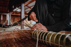 fokusera gammal kvinna med traditionell vietnamesisk klänning ao ba ba att göra, slå in tet tårta, det vietnamesiska månnyåret tet mat utomhus för händer. foto