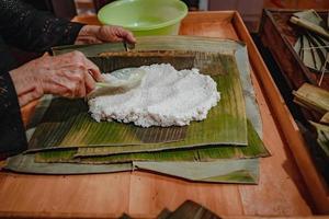 fokusera gammal kvinna med traditionell vietnamesisk klänning ao ba ba att göra, slå in tet tårta, det vietnamesiska månnyåret tet mat utomhus för händer. foto