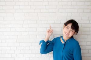 vackert porträtt ung asiatisk kvinna glad pekar med kopia utrymme på cement betong bakgrund, flicka leende står och visar framtid eller planering med budskap om dig. foto