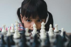 asiatisk liten flicka som spelar schack hemma. ett parti schack foto