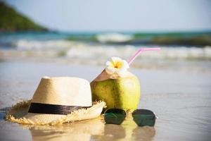 färsk kokosnöt med hatt och solglasögon på ren sandstrand med havsvågbakgrund - färsk frukt med havssandsolsemesterbakgrundskoncept foto