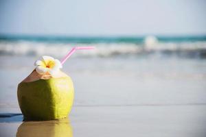 färsk kokosnöt med plumeria blomma dekorerad på ren sandstrand med havsvågbakgrund - färsk frukt med havssand sol semester bakgrundskoncept foto