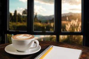 kaffe arom i kopp frukost morgon drink på träbord i café butik med anteckningsblock restaurang bakgrund foto