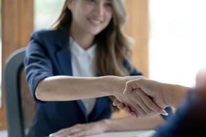 närbild av oigenkännlig glad affärskvinna skakar hand med affärspartner efter att ha undertecknat kontrakt under möte på kontoret. foto
