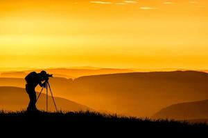 en professionell fotografs siluett är fokuserad på att fotografera på en vacker äng. foto