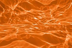 oskärpa suddig genomskinlig orange färgad klar lugn vattenyta textur med stänk och bubbla. trendiga abstrakt natur bakgrund. vattenvåg i solljus med kopia utrymme. blå akvarell konsistens foto