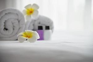 hotellhandduk och schampo och tvålbadflaska på vit säng med plumeria-blomma dekorerad - koppla av semester på hotellresortskonceptet foto