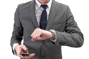 affärsman kontrollerar tiden på hans armbandsur och håller mobiltelefon isolerad på vit bakgrund. foto