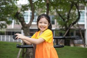 asiatisk glad tjej med orange klänning spelar på lekplatsen. foto