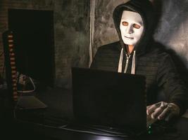 datorhacker - man i huvtröja med mask stjäl data från laptop foto