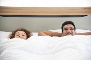 älskare koncept. unga attraktiva par liggande under vit filt i sängen foto