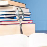 stack bok med förstoringsglas på trä skrivbord i informationsbibliotek av skolan eller universitetet, koncept för utbildning, läsning, studier, kopiera utrymme på blå bakgrund. foto
