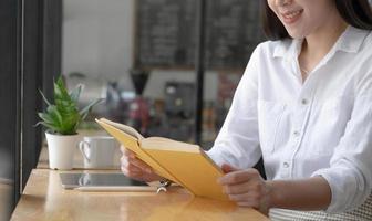 attraktiv ung asiatisk kvinna slappnar av att sitta i kaféet och njuta av att läsa sin favoritbok. foto