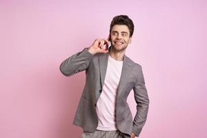 glad ung man i kostym pratar i mobiltelefon medan han står mot rosa bakgrund foto