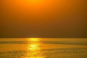 solen gick ner på kvällen. lysande gyllene färg som reflekterar havsvattnet foto