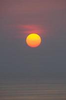 solen faller i havet. , himlen är orange och havet är mörkt foto