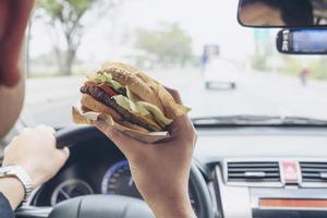 man kör bil medan han äter hamburgare foto